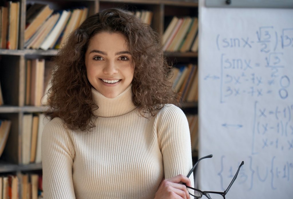 Confident smiling hispanic woman teacher looking at camera in classroom.